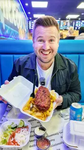 The creator visits a newly opened Mr. Cod takeaway in Woodley, highlighting its modern interior design, graffiti art, and menu offerings. He interacts with the staff and performs a taste test of the burger and masala fish, providing a positive review of the experience.