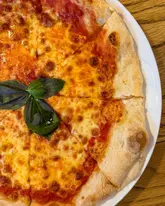 A top-down, close-up shot of a Margherita pizza served on a white plate on a wooden table. The pizza features melted mozzarella, tomato sauce, and fresh basil leaves.