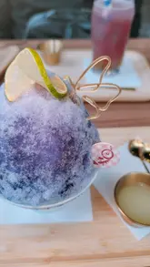A short-form video showcasing a new menu at a dessert cafe, featuring close-up shots of bingsu, tofu pudding, sandwiches, and a fried snack platter. The video uses text overlays to describe the items and highlights the visual appeal of the food, particularly a color-changing bingsu.