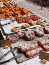 A clear, well-lit, and appetizing photograph of a bakery display case filled with a variety of freshly baked savoury and sweet pastries, including curry beef croissants and danishes, with clear labels for the items.