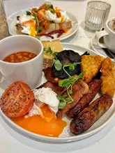 A standard, functional food photograph capturing a full English breakfast and avocado toast. The lighting and focus are competent, highlighting the textures of the food, though the composition suffers from tight cropping that cuts off the main plate.