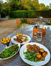 A high-quality, natural-light shot of a dinner spread at an outdoor venue. The image captures the atmosphere of an al fresco meal, though the table arrangement is cluttered with non-food items.
