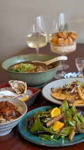 A montage of various Taiwanese dishes and drinks at Wine The Noodles, featuring close-ups of noodles, oysters, salad, and a cocktail.