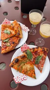An overhead, flat-lay style shot of pizza slices and drinks served on a metal mesh table at a rooftop venue.