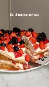 A short, visually appealing video demonstrating the assembly of a layered summer cake featuring sponge, meringue, whipped cream, and fresh berries. The video focuses on the texture and presentation of the dessert.