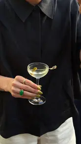 A short, aesthetic clip featuring a waiter pouring mini cornichon martinis from a pitcher into small glasses on a branded tray at Bar Antoine.