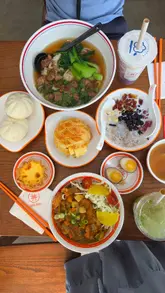 A montage of various dishes including a pineapple bun, egg tart, beef noodles, and a taro milk drink, filmed primarily from a top-down perspective at a cafe table.