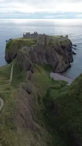 A single, continuous drone shot capturing the exterior of Dunnottar Castle, a medieval fortress situated on cliffs overlooking the North Sea in Scotland.