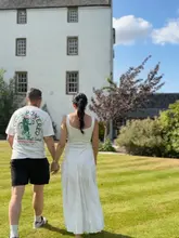 A bright, outdoor lifestyle shot of a couple walking hand-in-hand across a manicured lawn towards a large, historic white hotel building, effectively promoting a relaxing spa staycation.
