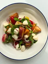 A vibrant, overhead shot of a fresh panzanella salad featuring tomatoes, mozzarella, peaches, and croutons on a clean white background.