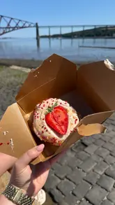 A short video showcasing The Little Bakery in Queensferry, featuring shots of the cafe interior, the display case filled with baked goods, and a close-up of a strawberry shortcake, followed by a scenic shot of the nearby Forth Bridge.
