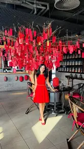 A professionally captured, high-quality photograph of a woman posing in a sophisticated, red-themed restaurant interior. The composition is balanced and clean, effectively showcasing the venue's elegant decor and upscale atmosphere.