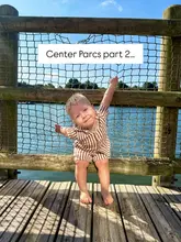 A bright, high-quality lifestyle shot of a toddler sitting on a wooden bridge over a lake at a Center Parcs holiday resort, capturing a family-friendly travel moment.