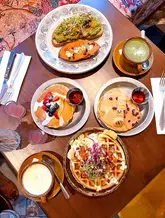 An overhead flatlay photograph of a brunch spread featuring avocado toast, pancakes, waffles, and drinks, arranged on a patterned table.