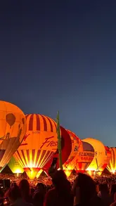 A visually striking night-time shot capturing the 'Night Glow' event at the Bristol Balloon Fiesta, featuring a line of illuminated hot air balloons against a clear twilight sky.