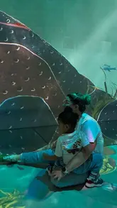 A photo of a parent and child sitting on the floor inside an immersive art gallery, surrounded by projected artwork.