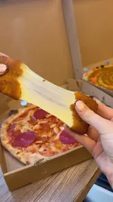 A close-up, high-impact shot of a mozzarella stick cheese pull, with a pizza box visible in the background, typical of a casual takeaway food review.
