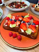 A vibrant, close-up shot of berry-topped French toast served on an orange plate, with other brunch dishes visible in the background, capturing a fresh and appealing cafe setting.
