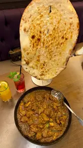 A montage video showcasing various dishes from Karahi by Sanam, including a mixed grill, lamb karahi, naan, drinks, and dessert, along with shots of the restaurant interior.