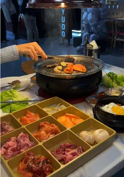 Group enjoying halal Korean BBQ at Tayudo in Chinatown, Birmingham, with a variety of meats and dishes on the table.
