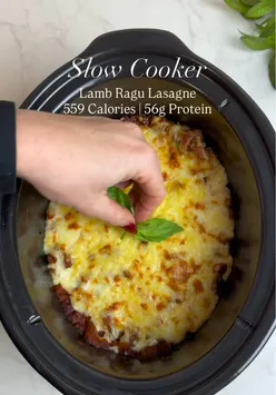 Comforting slow cooker lamb ragu lasagne with 56g protein per serving, topped with creamy cheese and fresh basil.