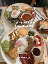 A top-down, flat-lay photograph of two brunch plates featuring a fusion-style full English breakfast, including halloumi, avocado, sausage, baked beans, and a samosa, accompanied by a latte. The image is overlaid with text identifying the location as a favourite brunch spot.