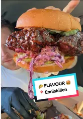 A creator reviews food from a takeaway spot called Flavour in Enniskillen, sampling tacos, loaded fries, and a Korean-style burger while sitting in their car.